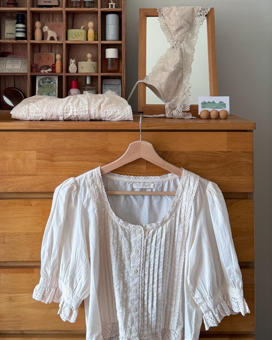 White lace top on a hanger in front of a wooden dresser with decorative items.